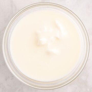 Overhead view of a glass bowl filled with creamy white buttermilk on a light marble surface, illustrating buttermilk substitutes.