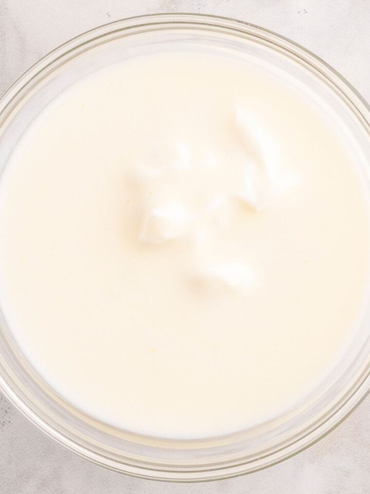 Overhead view of a glass bowl filled with creamy white buttermilk on a light marble surface, illustrating buttermilk substitutes.