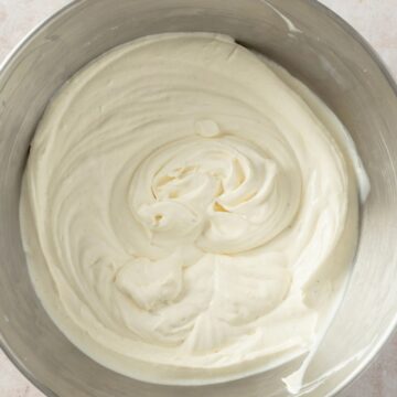 Overhead view of thick, freshly whipped cream with soft swirls in a stainless steel mixing bowl.
