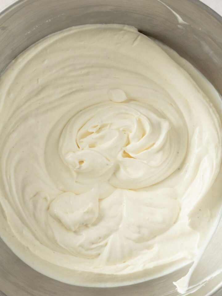 Overhead view of thick, freshly whipped cream with soft swirls in a stainless steel mixing bowl.