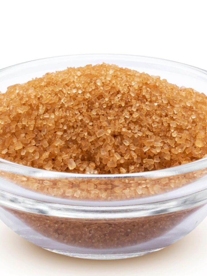 Glass bowl filled with coarse brown sugar crystals on a white background, illustrating brown sugar substitutes for baking.