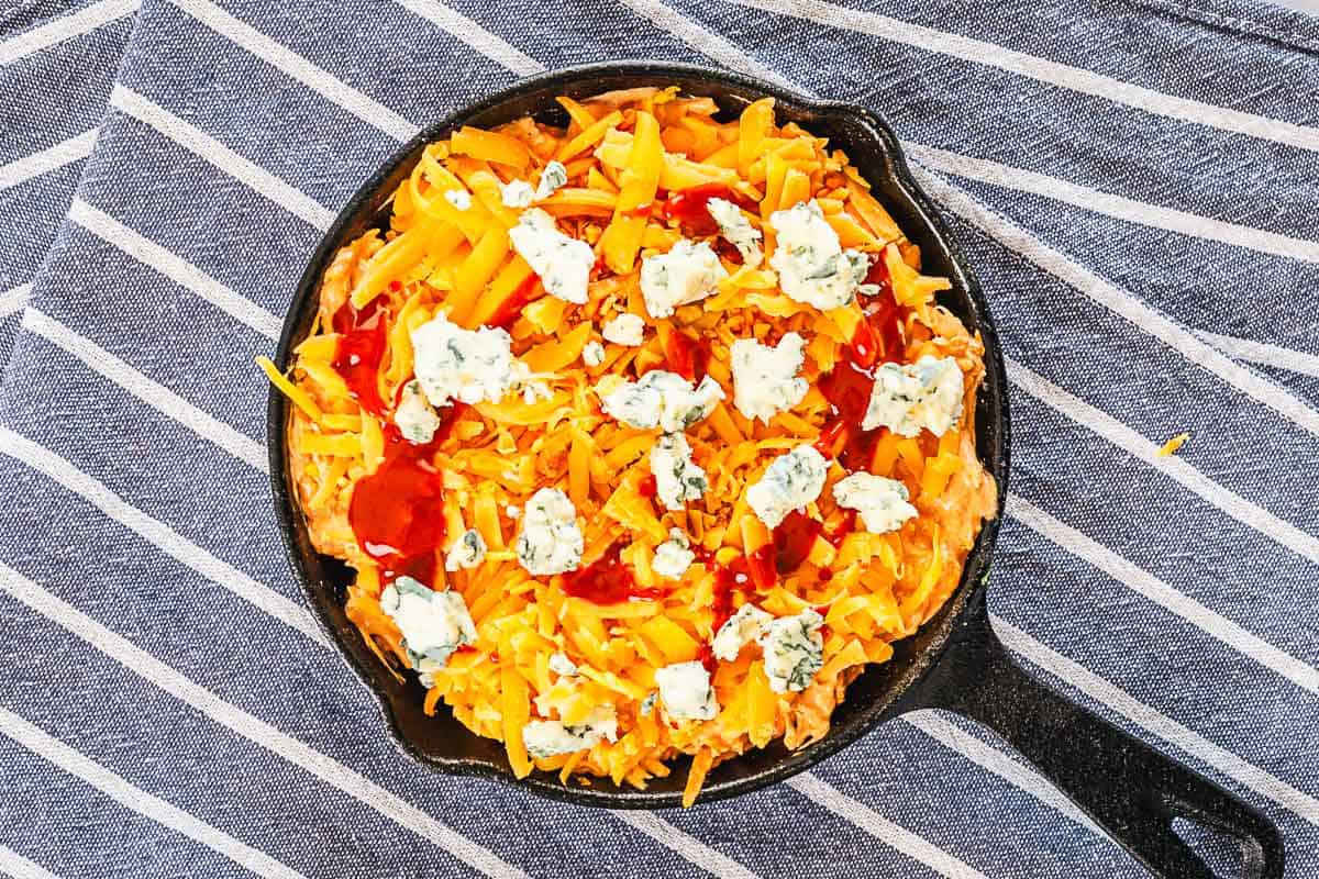 buffalo chicken dip topped with crumbled blue cheese, cheddar cheese and drizzled with hot sauce before baking
