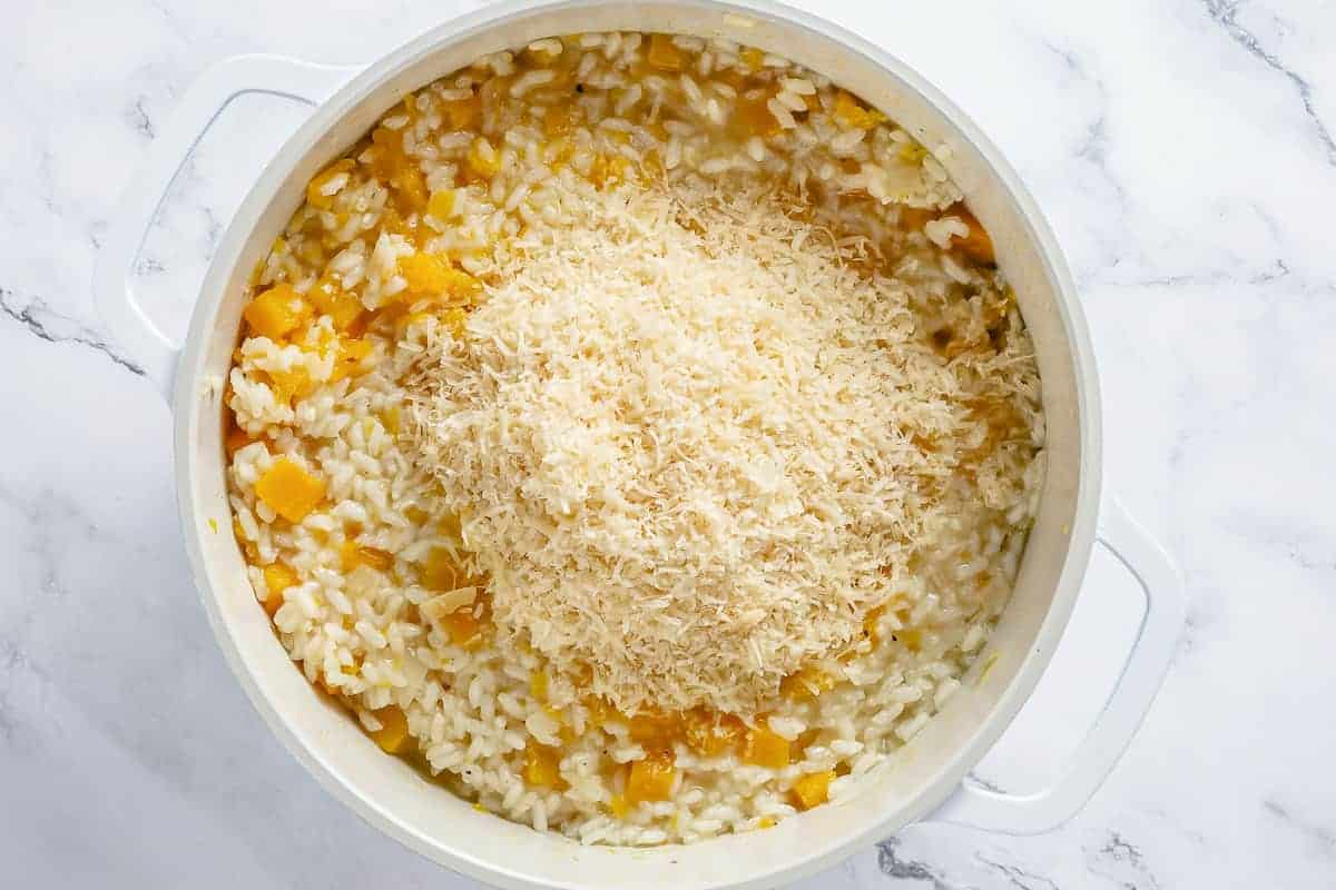 parmesan cheese on top of pumpkin risotto ingredients simmering in a white pot