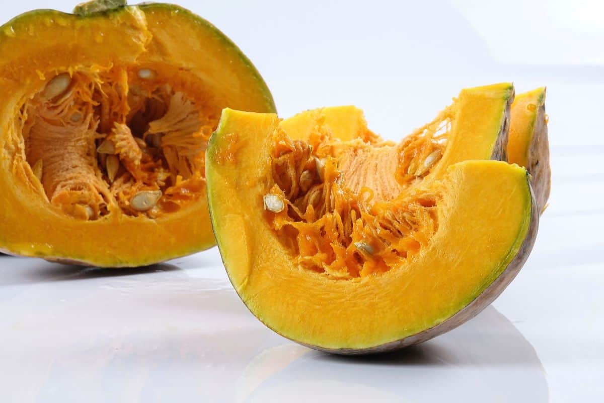 Cut kabocha squash showing bright orange flesh, seeds, and green skin.