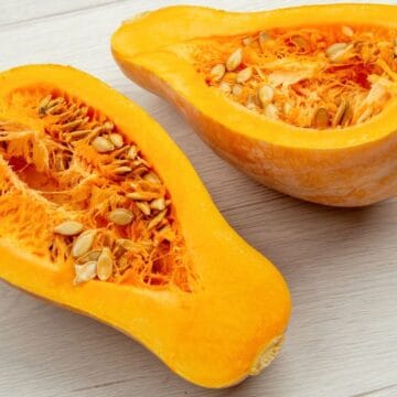 Halved butternut squash with seeds and bright orange flesh on a light wooden surface.