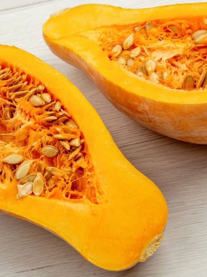 Halved butternut squash with seeds and bright orange flesh on a light wooden surface.