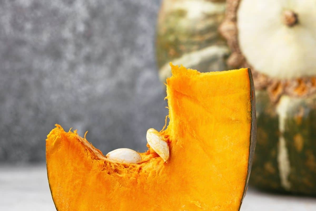 Cut buttercup squash wedge showing bright orange flesh and seeds, with whole buttercup squash in the background.