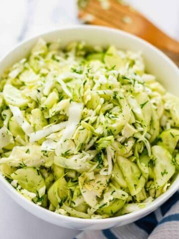 Cabbage Salad in a white bowl angle view shot with a wooden spatula behind it