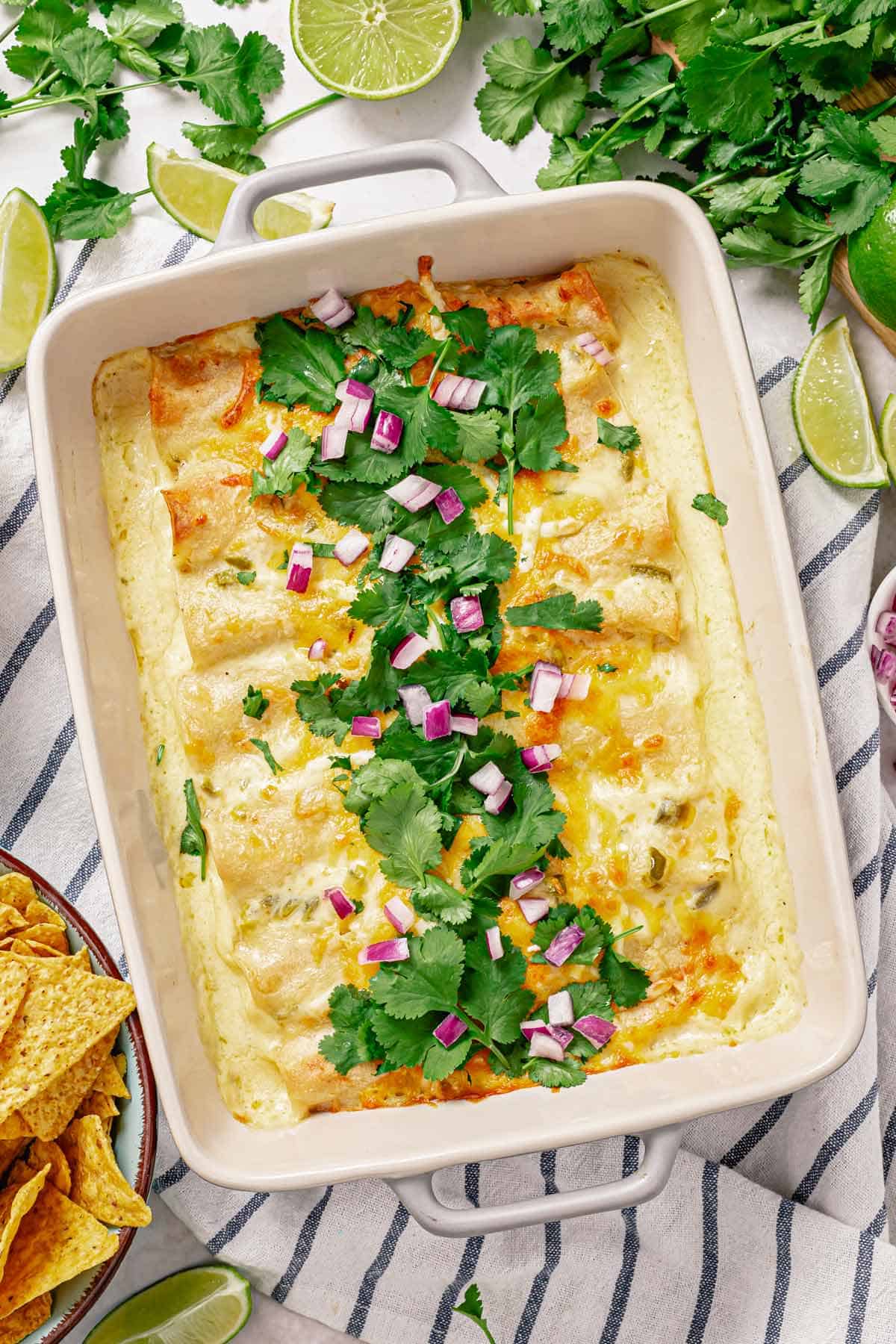 an over head shot of chicken enchilada in white sauce in a baking dish garnished with cilantro leaves and diced red onion in the middle