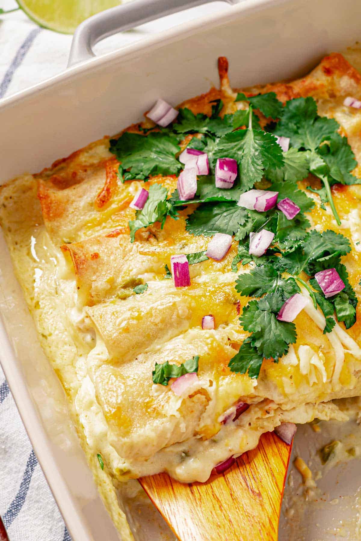 chicken enchiladas in a baking dish with a wooden spatula