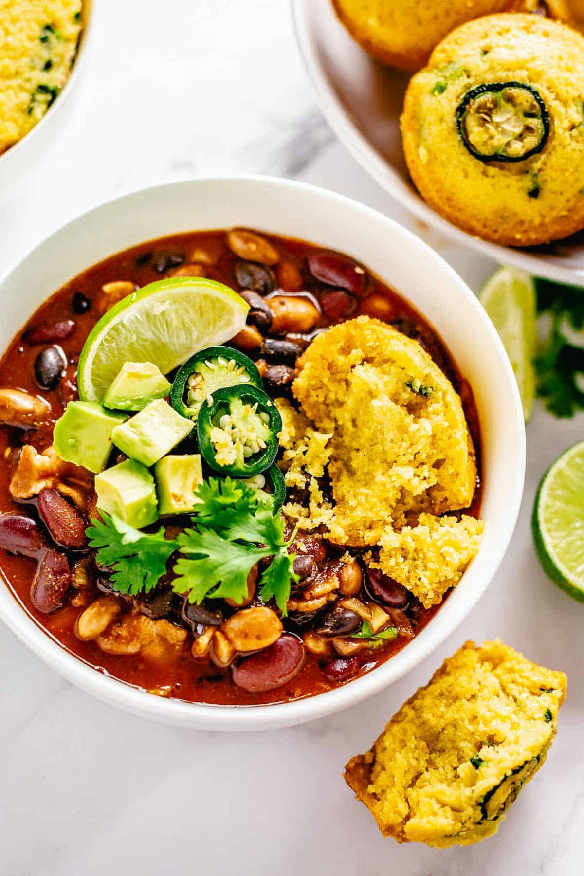 cooked beans in red sauce in a bowl with cornbread muffins and jaalpeno, cornbread, lime toppings