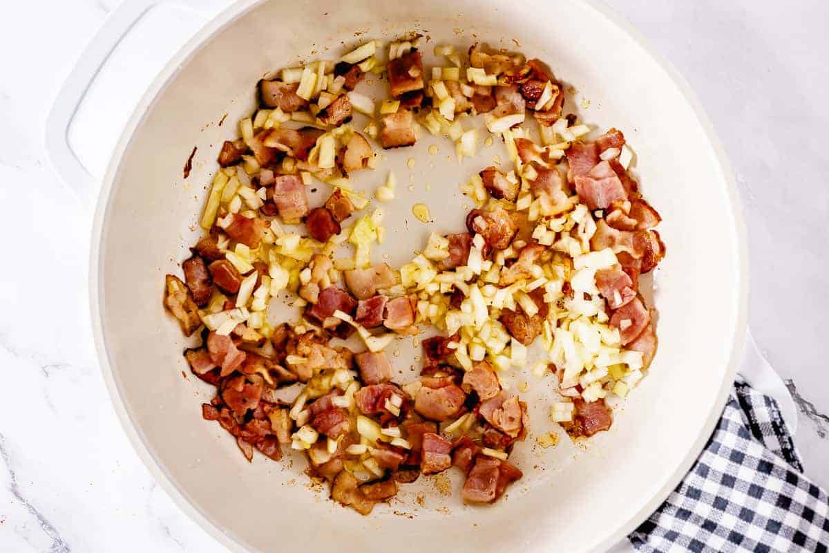 Onion and bacon sauteeing in a white pot
