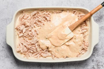 white sauce spreaded over shredded chicken in casserole