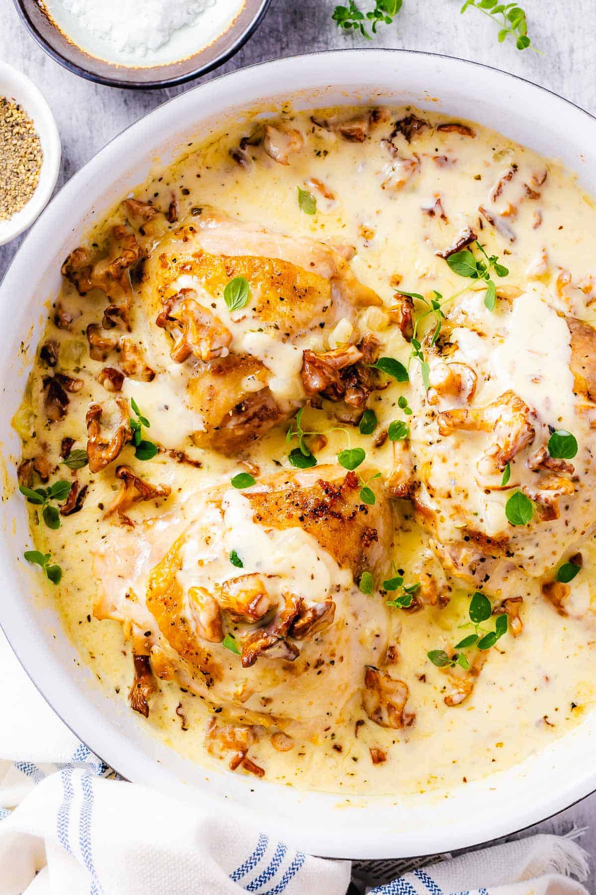 top down shot of a white skillet with chicken thighs in creamy mushroom sauce