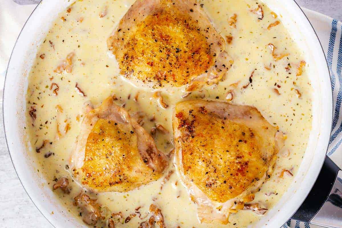cooked chicken thighs in a pan with creamy mushrooms sauce