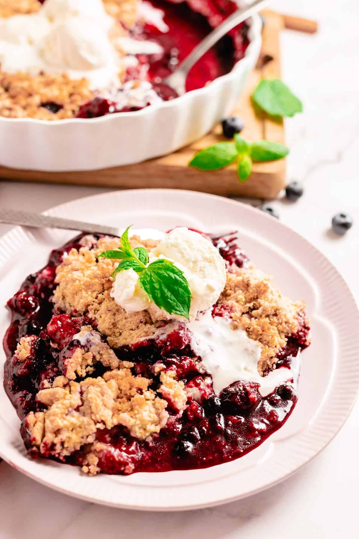 mixed berry crumble in a white round baking dish with mint leaf and ice cream