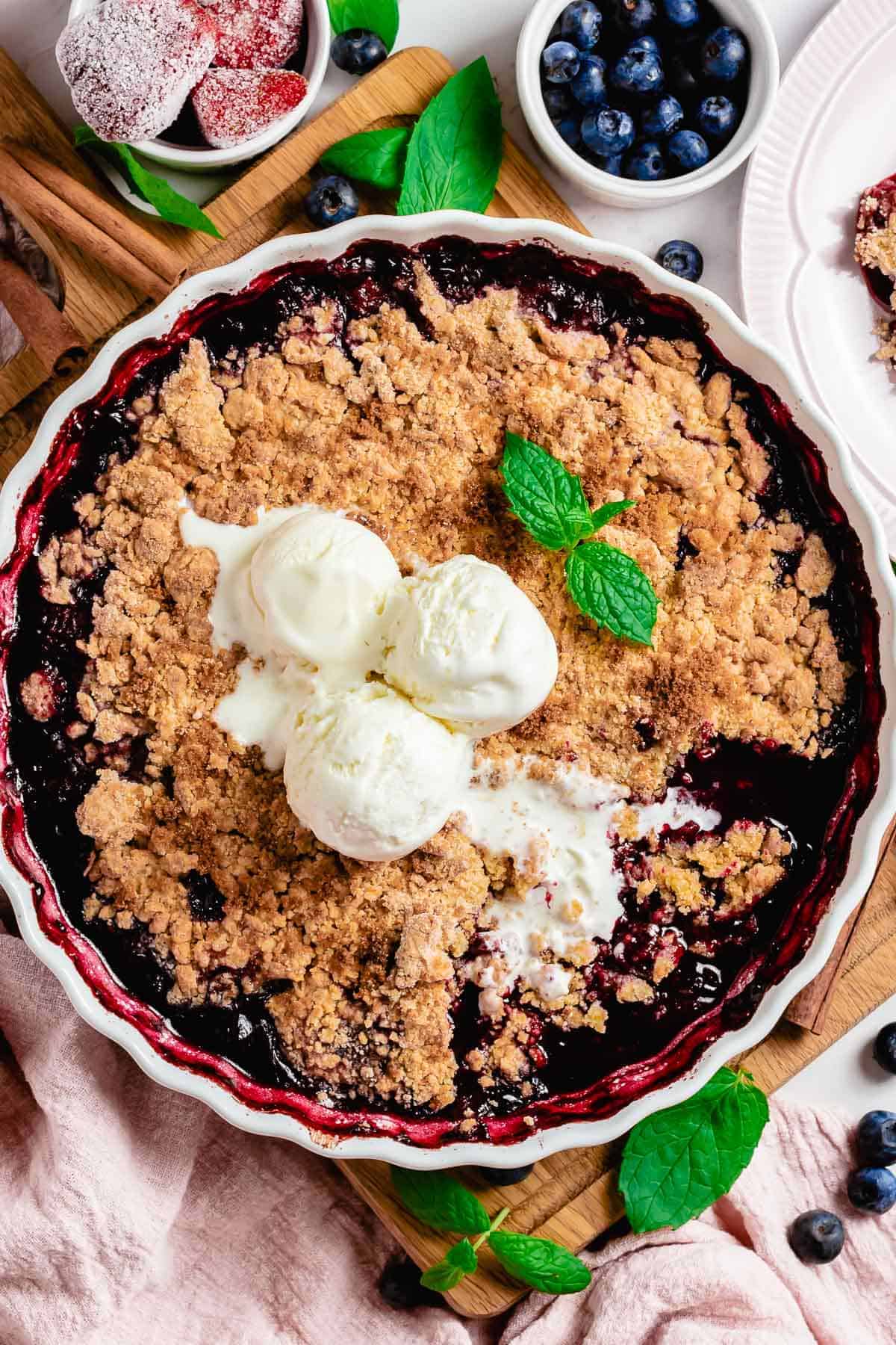 mixed berry crumble in a white round baking dish with mint leaf and ice cream