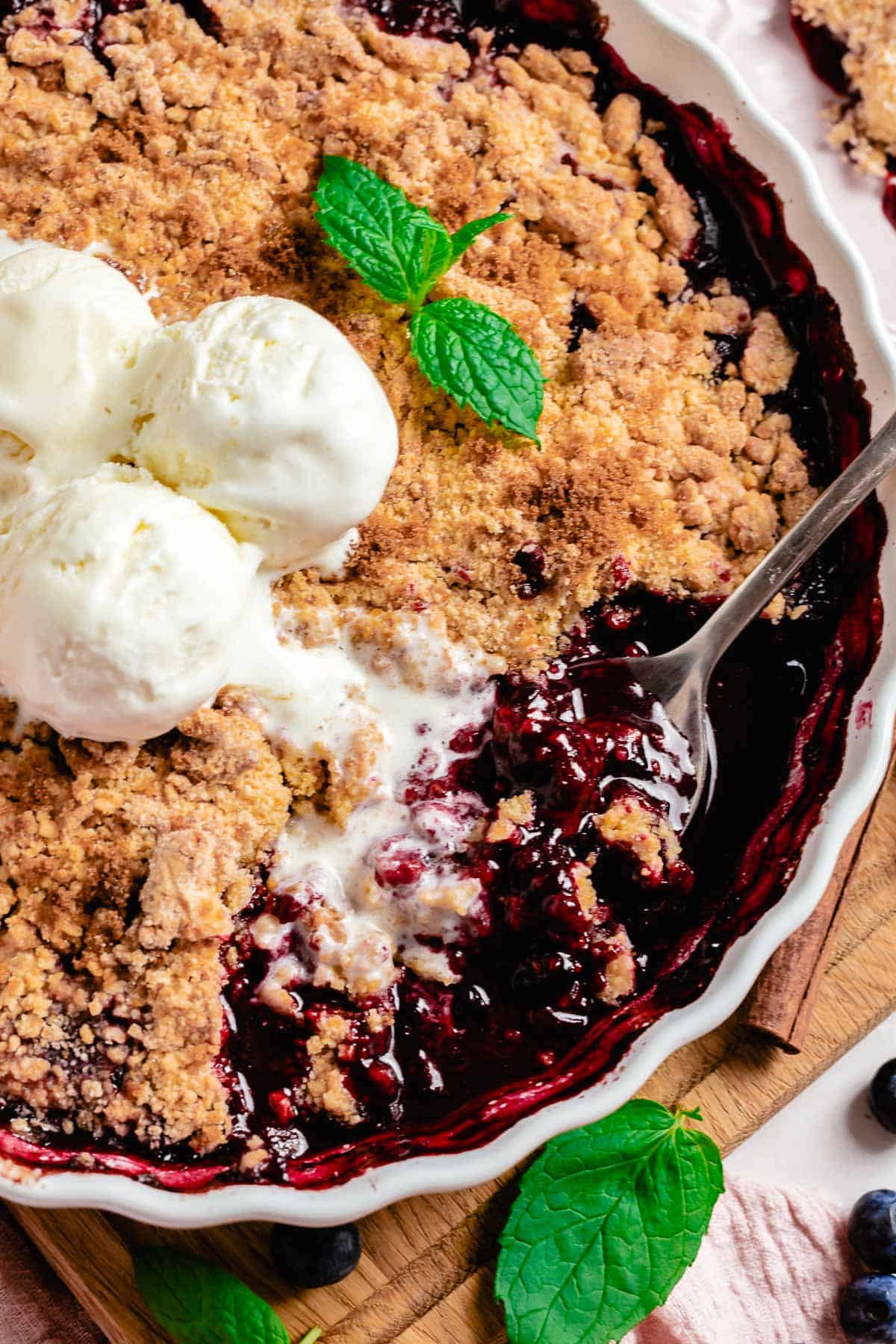 mixed berry crumble with ice cream and a spoon taking a piece out of baking dish