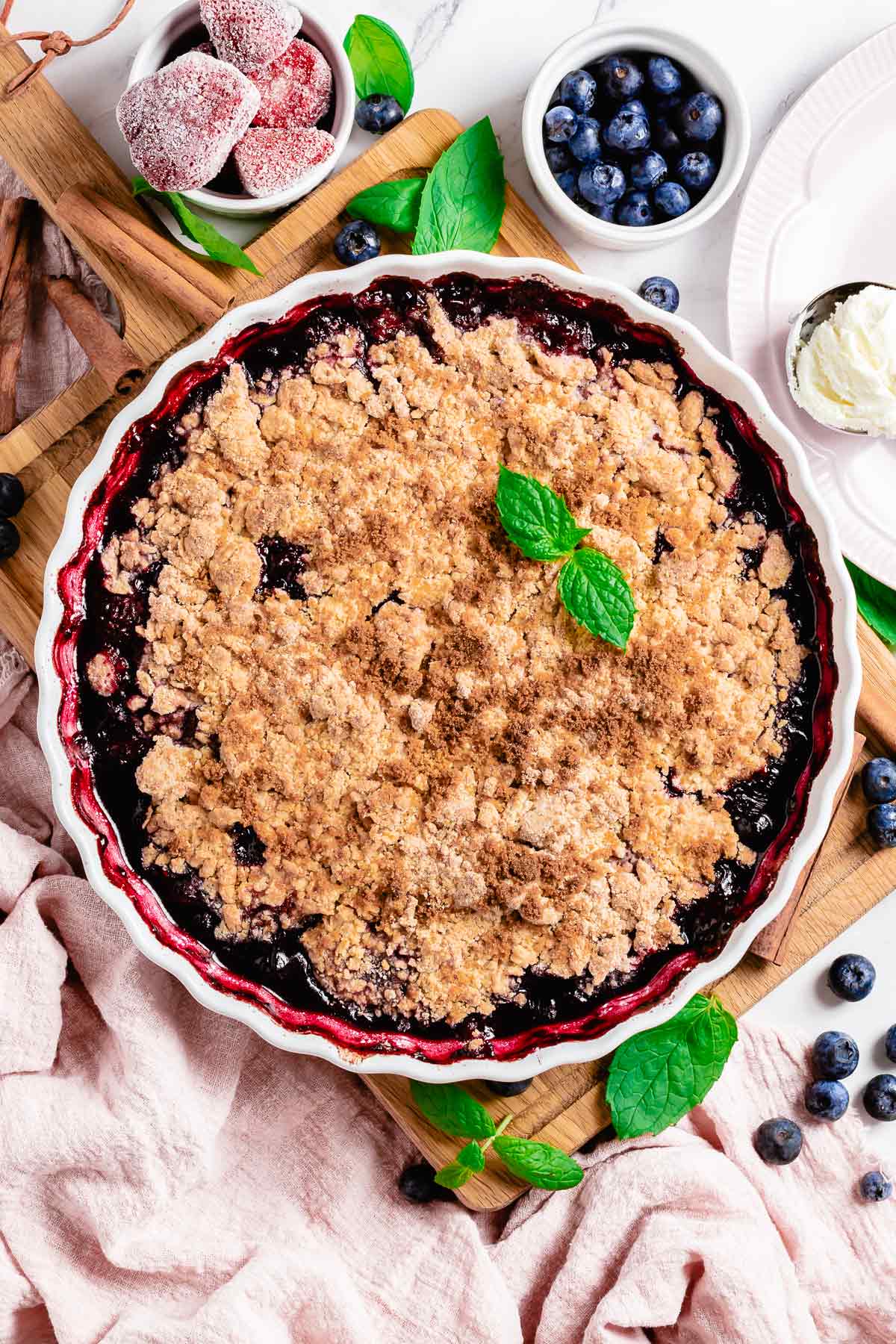 mixed berry crumble in a white round baking dish with mint leaf