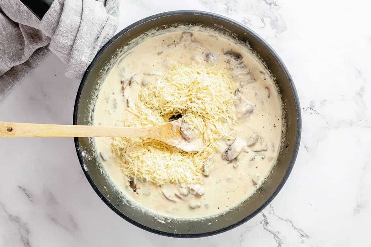 Parmesan cheese stirred into the creamy mushroom sauce in a black skillet