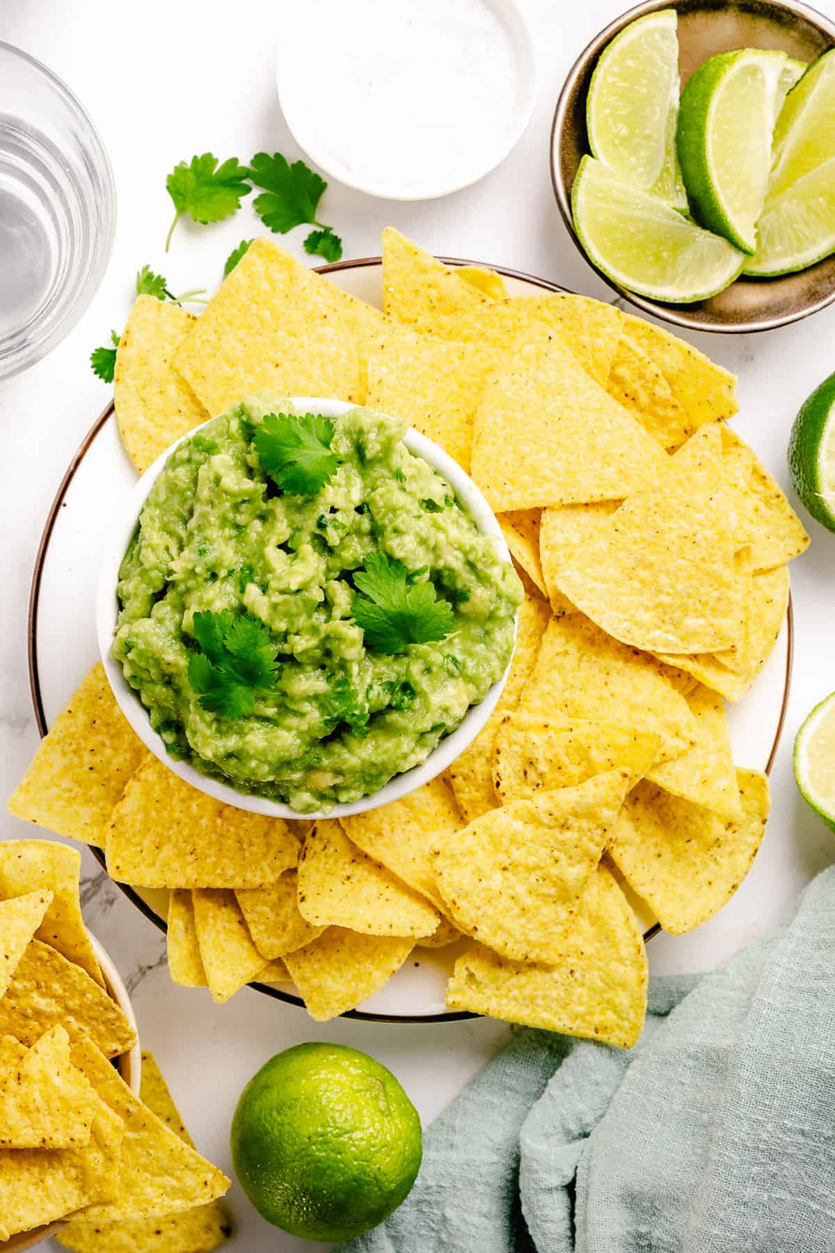 Simple guacamole in a small bowl surrounded with nacho chips flatlay on a marble background
