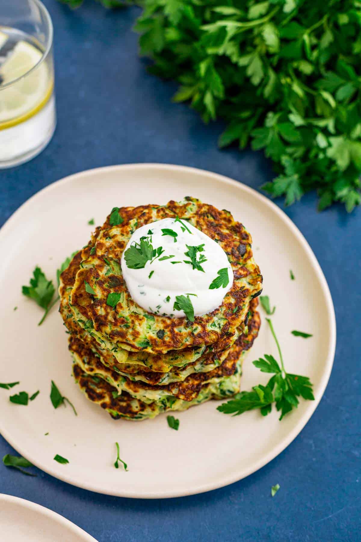 stack of zucchini fritters with a dollop of sour cream and parsley