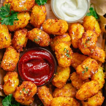 head shot of piled tater tots with a bowl of ketchup and mayonnaise