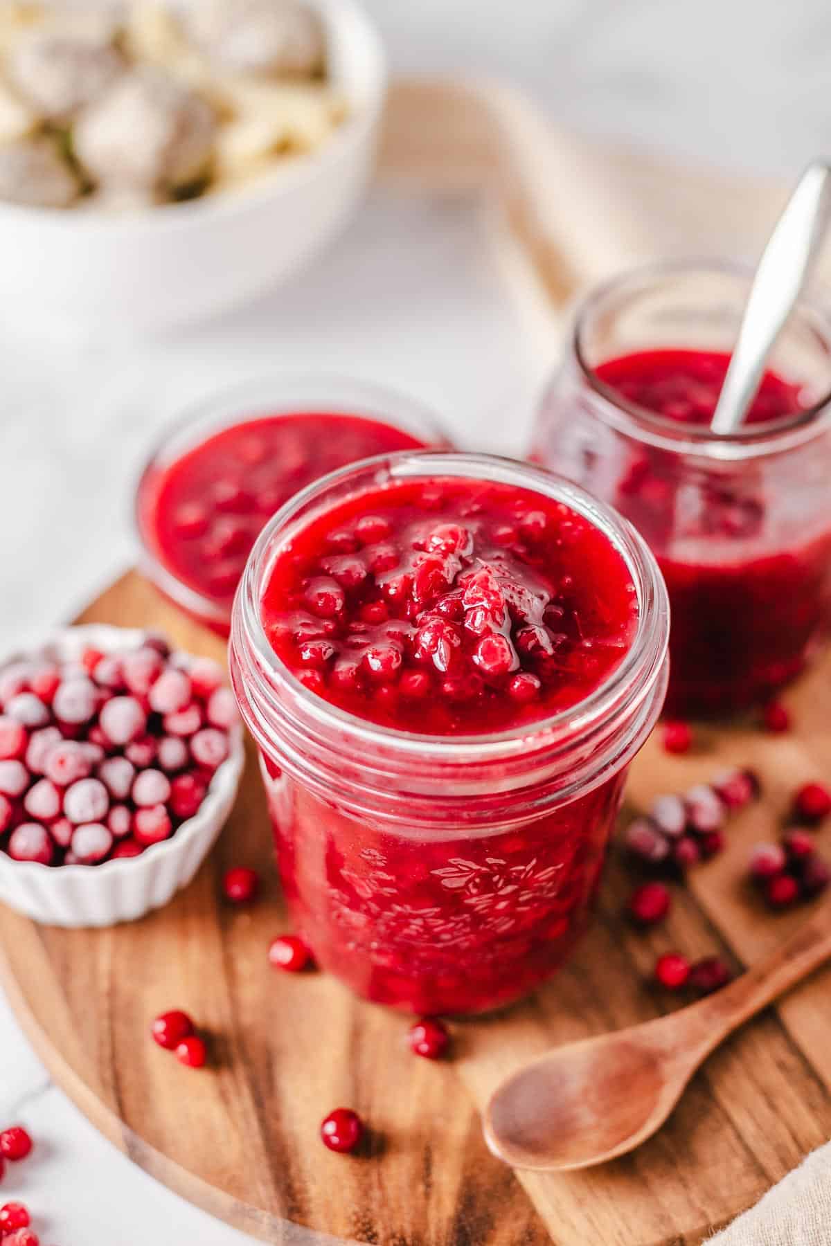 lingonberry sauce in a glass jar with frozen berries in the background
