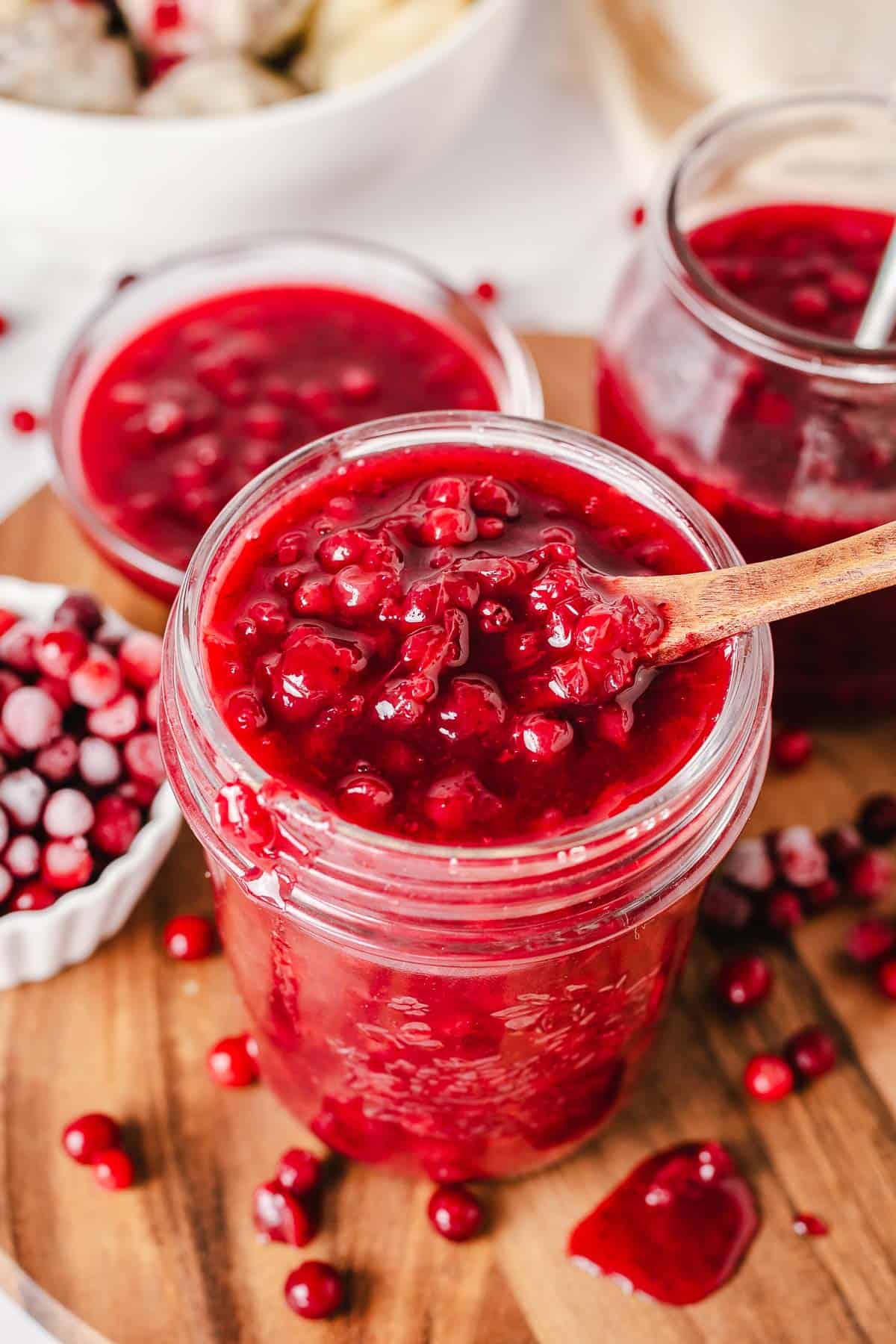 lingonberry sauce in a glass jar close up shot with frozen berries in the background
