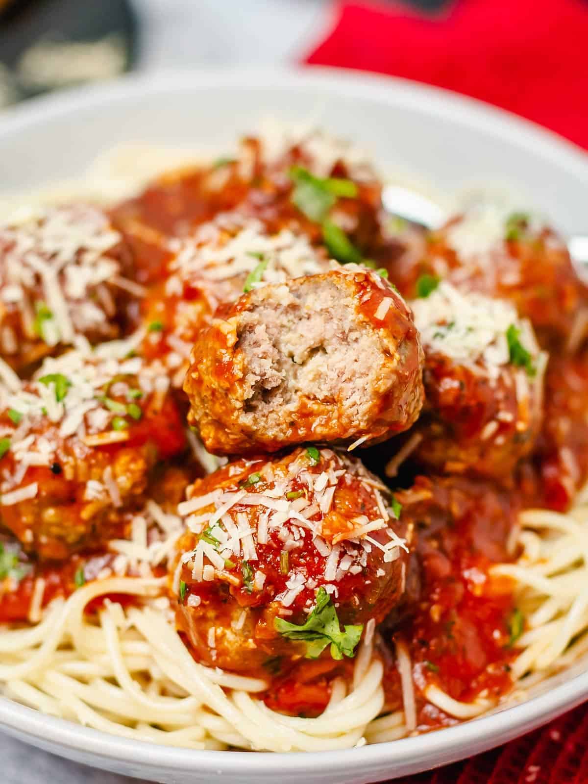 stacked meatballs in tomato sauce on a pile of spaghetti, bite shot of a top centered meatball