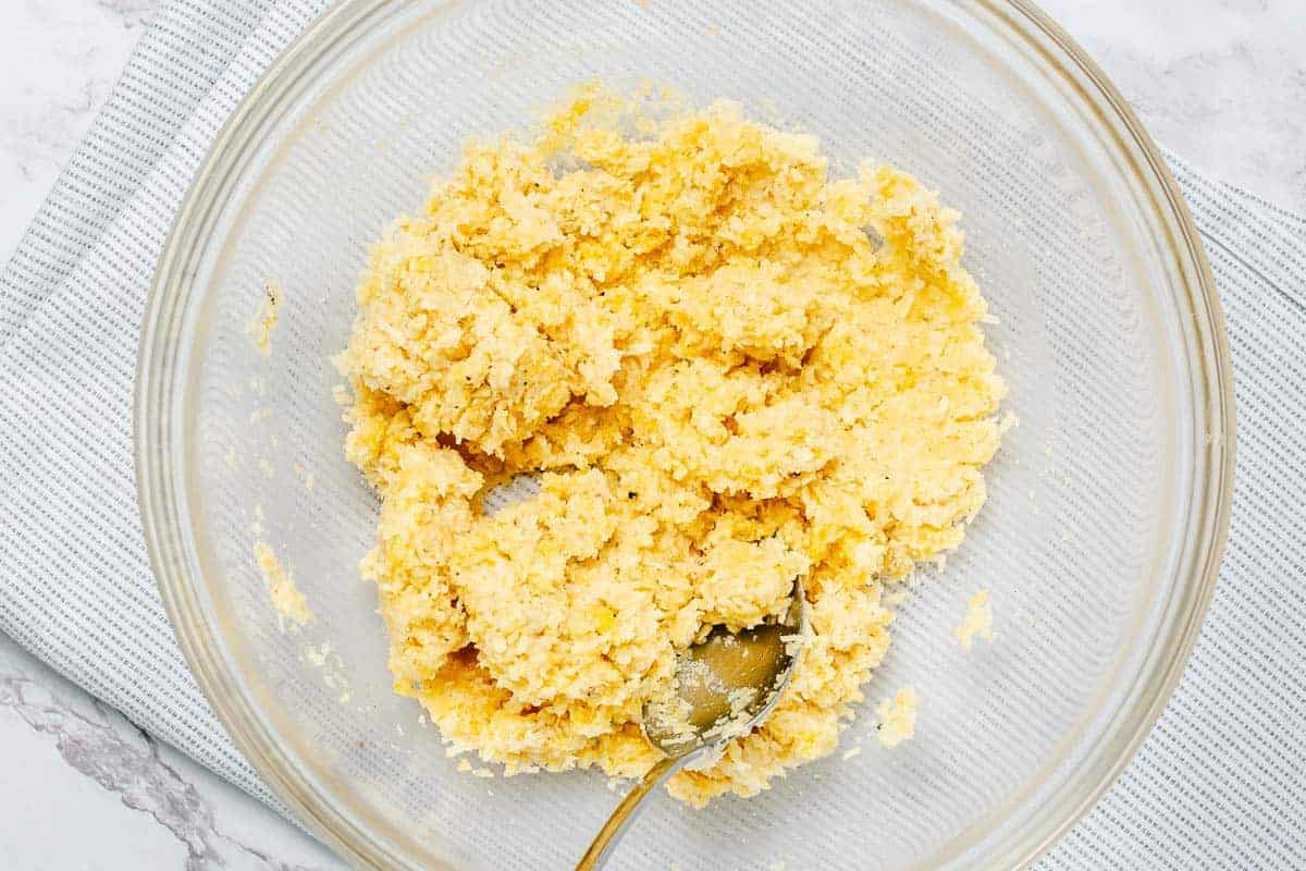 flatlay shot of seasonings, parmesan cheese, breadcrumbs and egg mixed in a large transparent glass bowl