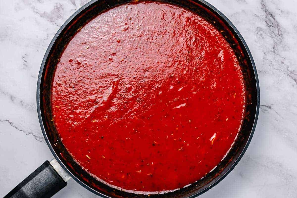 shot of a simmering homemade tomato sauce in a large black skillet