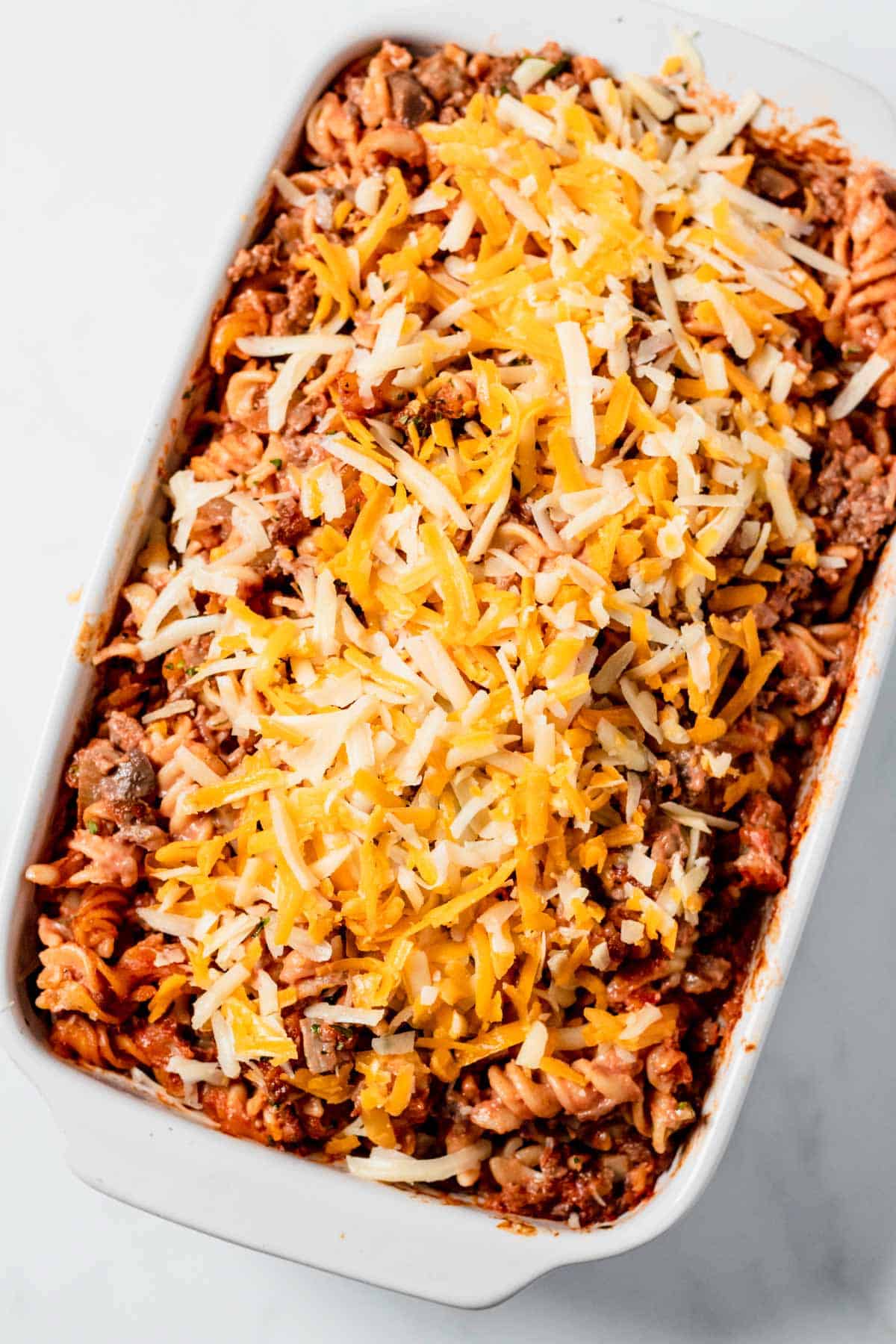 pasta casserole topped with cheese before baking