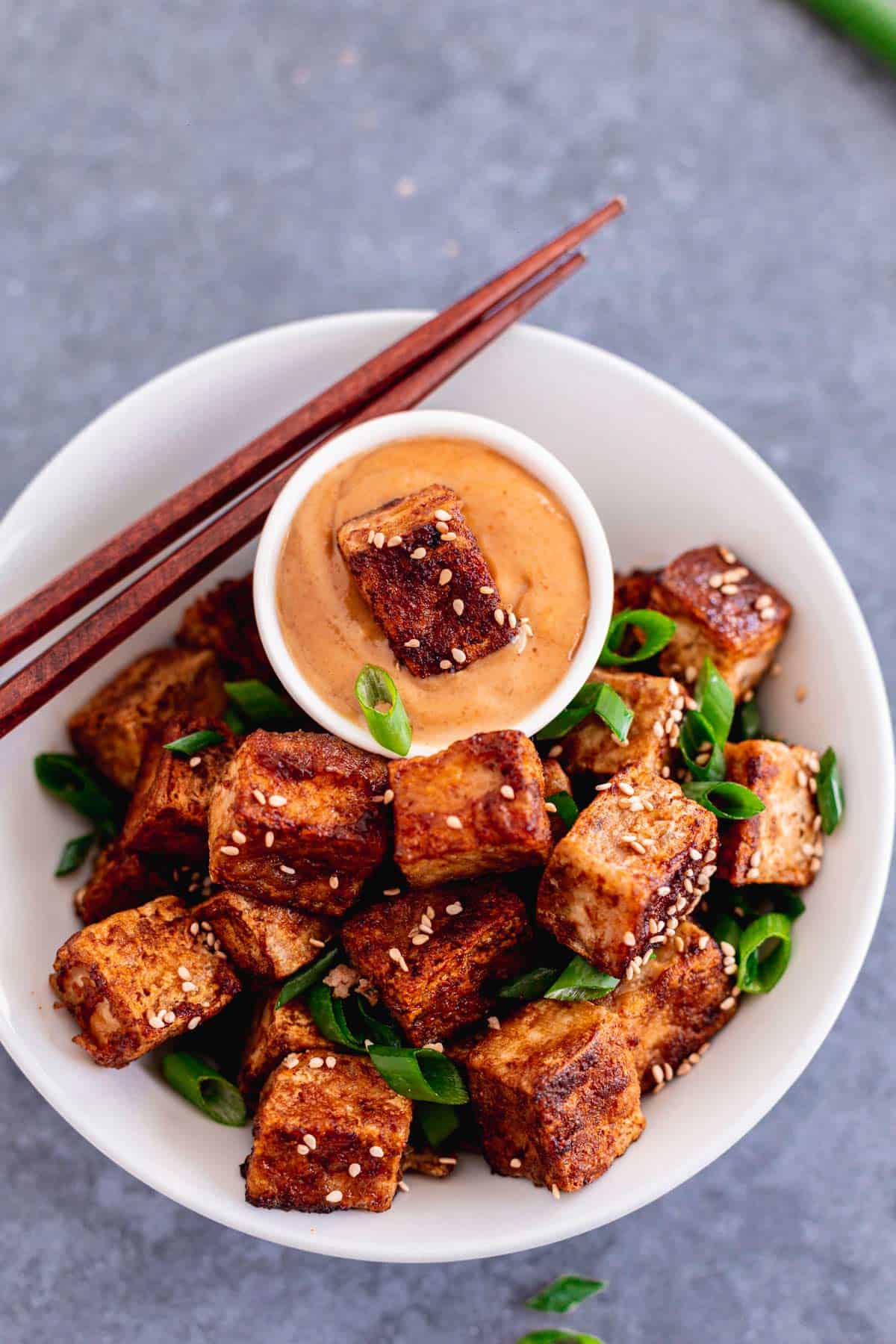 pan fried crispy tofu in a bowl with scallions and peanut sauce