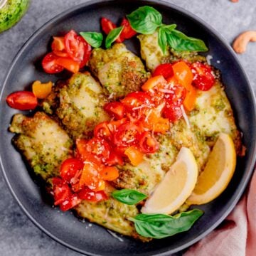 air fryer tilapia with pesto in a plate with cherry tomatoes and parmesan