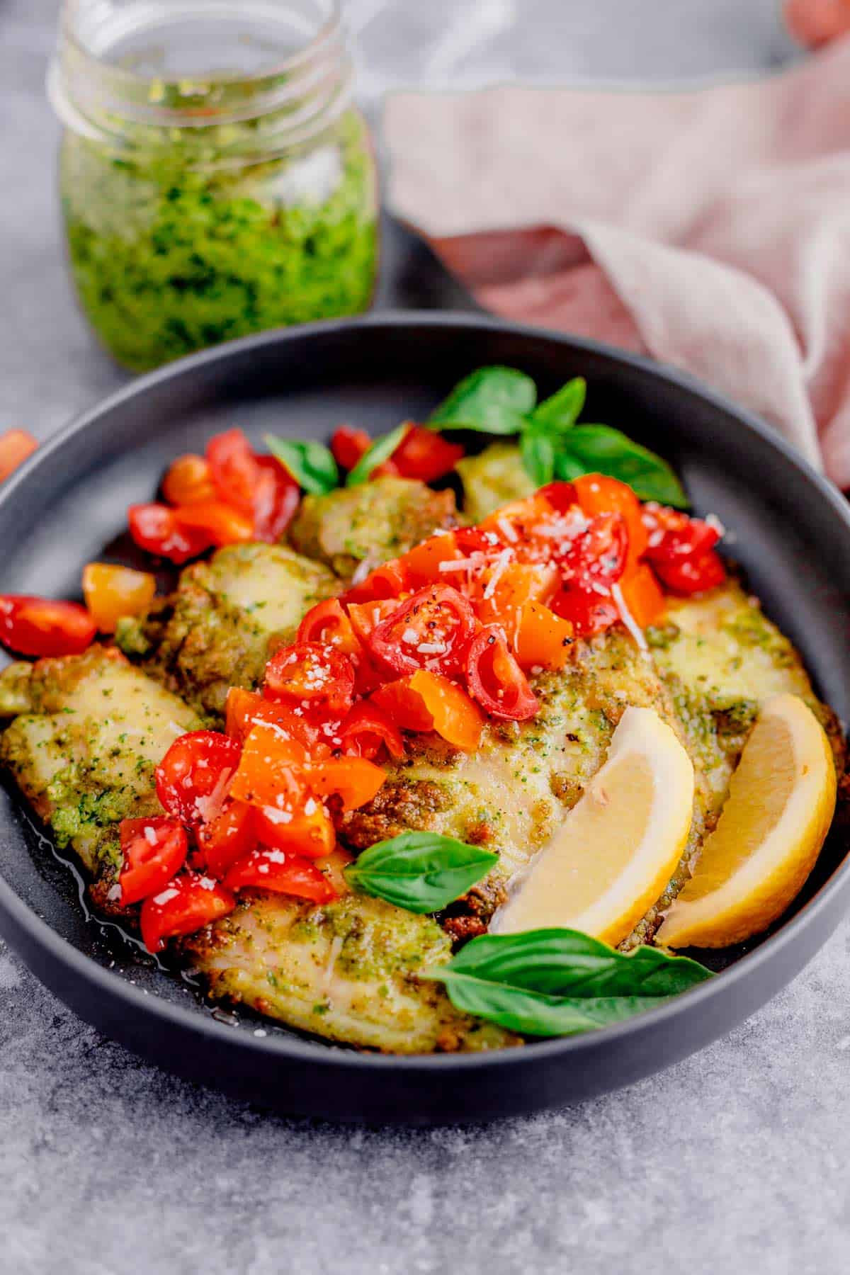 air fryer tilapia with pesto in a plate with cherry tomatoes and parmesan