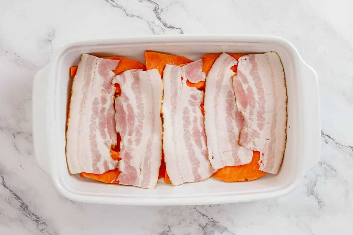 Pumpkin and bacon strips in a white casserole dish on a marble table.