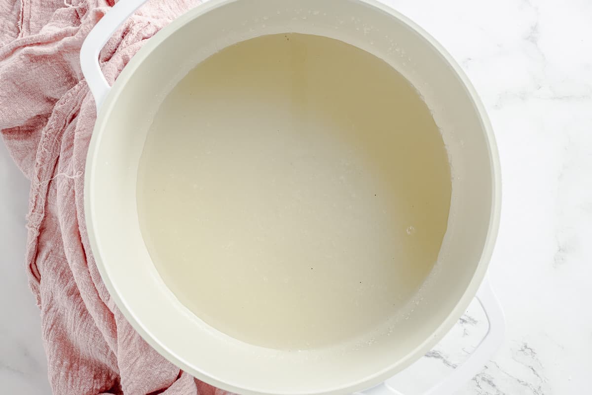 Sugar and water melted in a white heavy-bottomed pot with a pink towel as a prop.