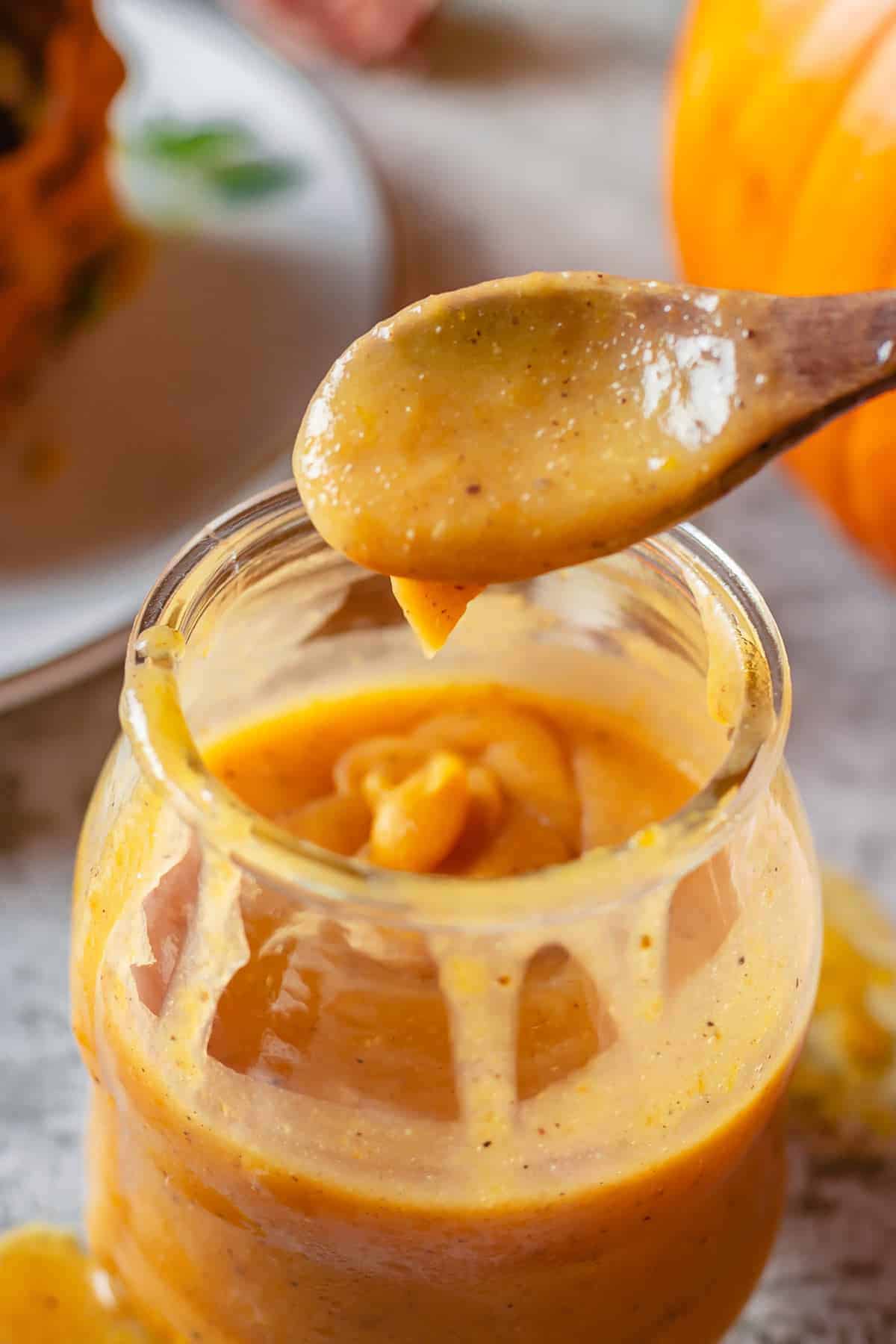 close up shot of pumpkin caramel ina  glass jar with a wooden spoon drizzle