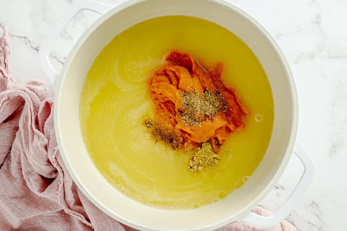 pumpkin puree and spices added to a white large pot along with melted sugar and butter