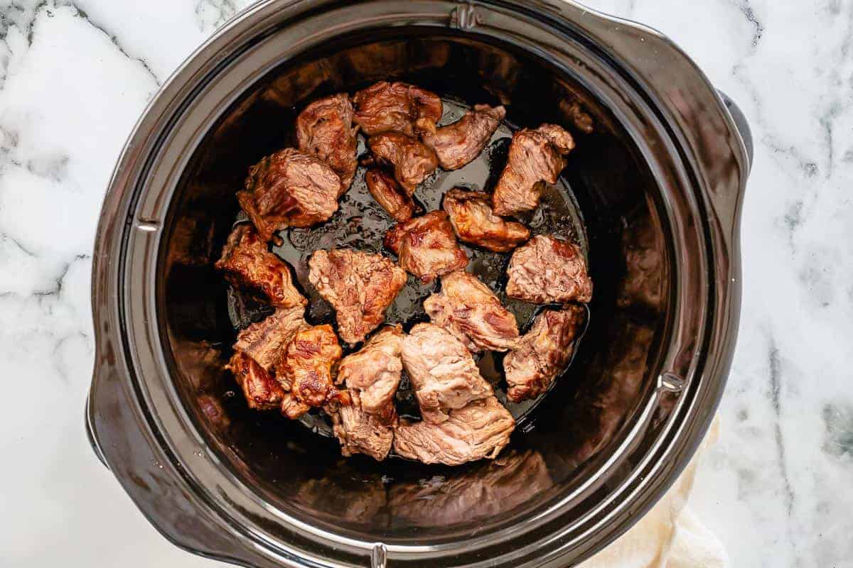seared beef chunks in a pot of a slow cooker
