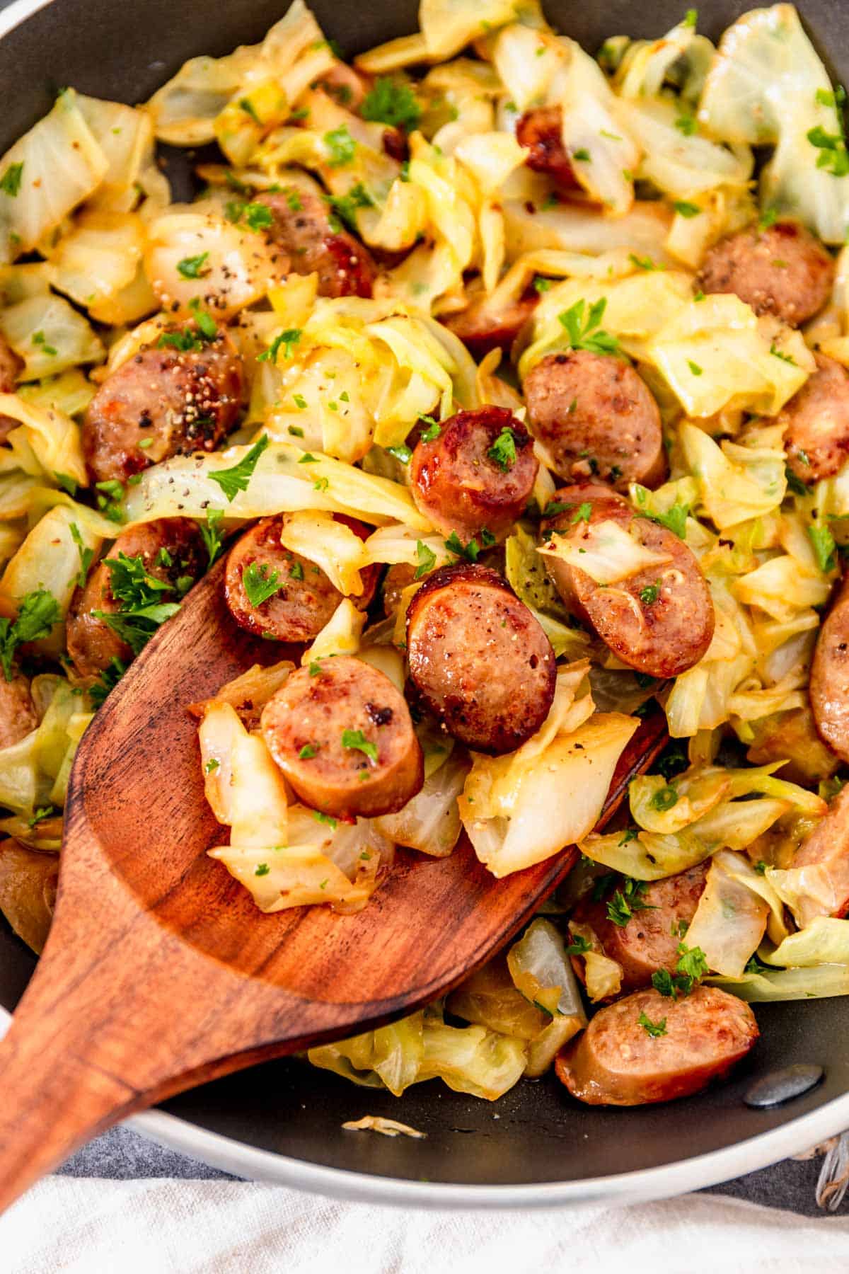 a wooden spoon in the cabbage with sausage skillet