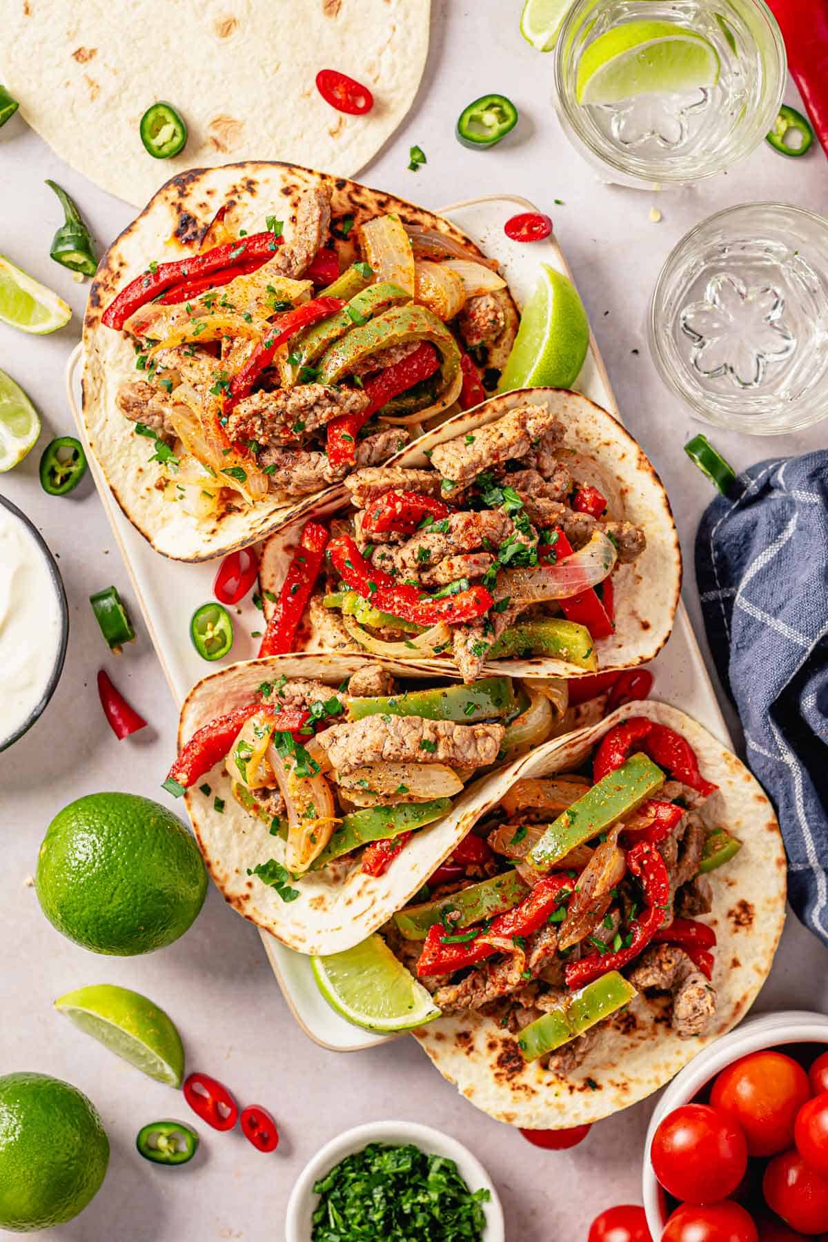 steak fajita tacos in a row with toppings and garnishes