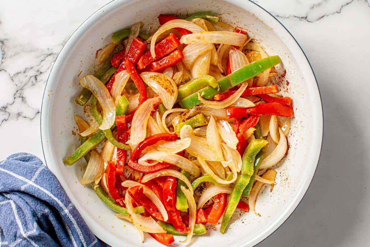 onions and bell peppers saute in a white skillet