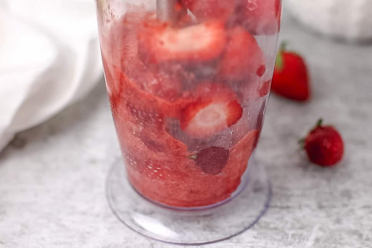 Strawberries in a blender cup on a grey background