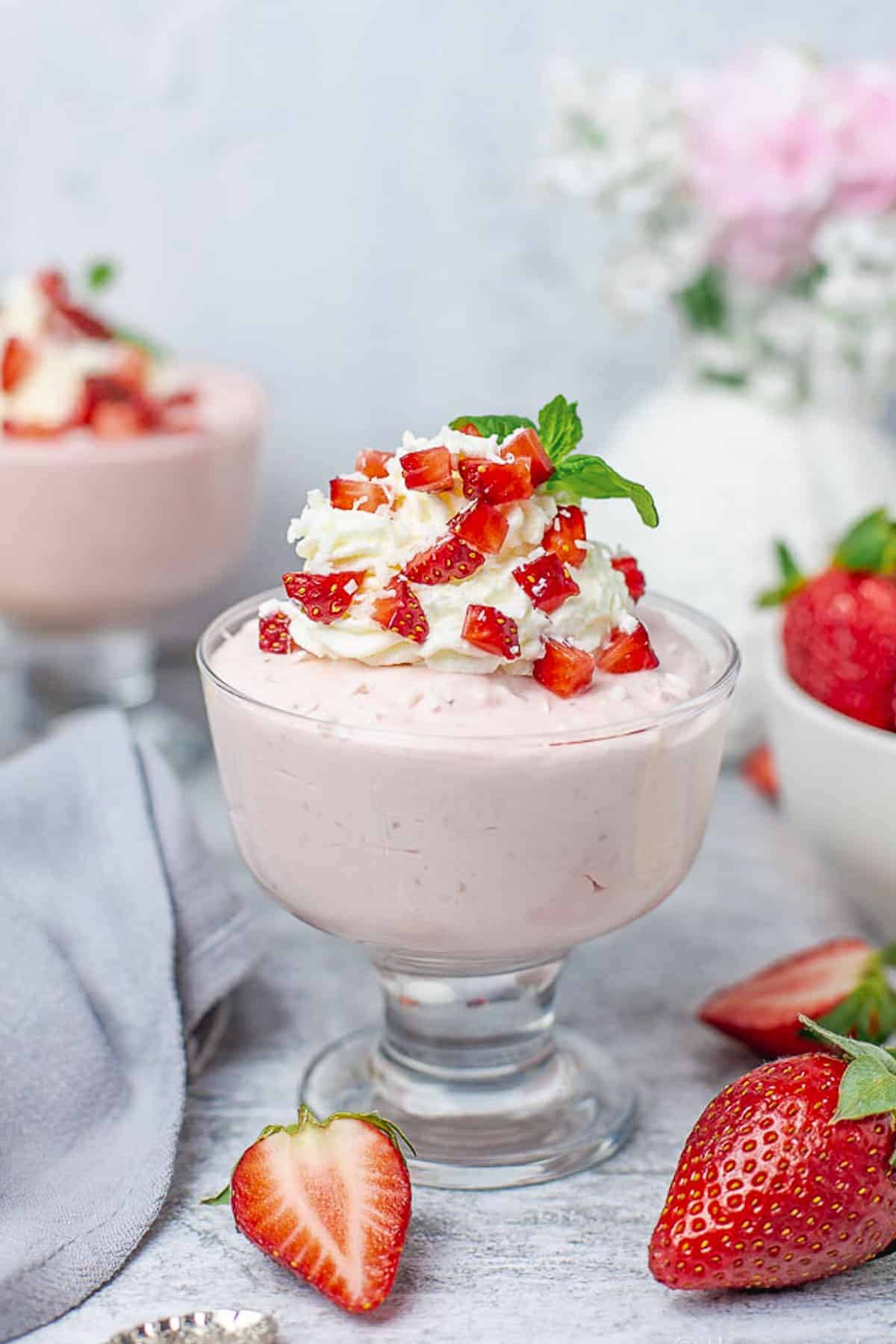 Strawberry Mousse in a glass cup with whipped cream and strawberries on a grey background