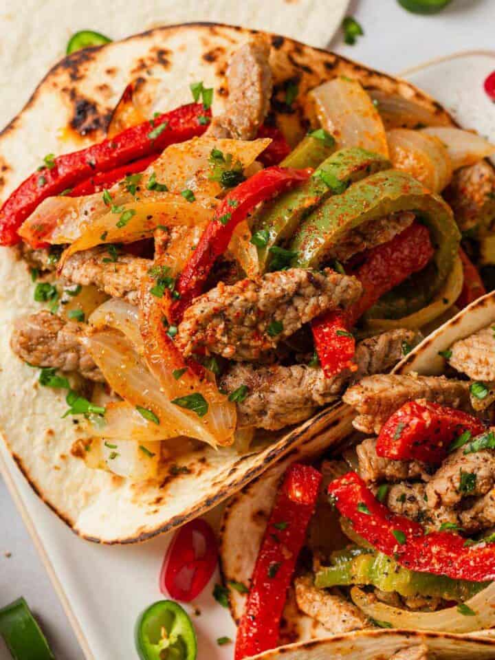 steak fajita tacos in a row with toppings and garnishes