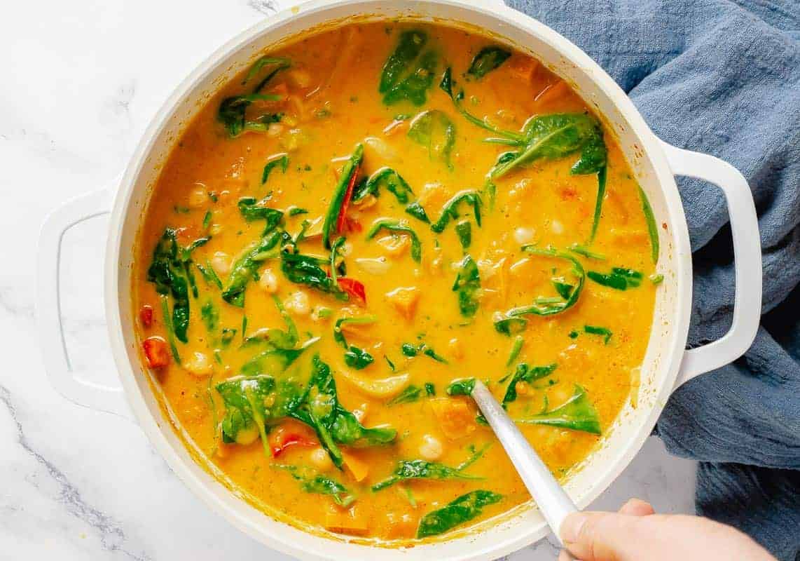 stirring with a spoon ready made pumpkin curry with coconut milk, chickpeas, spinach and peppers