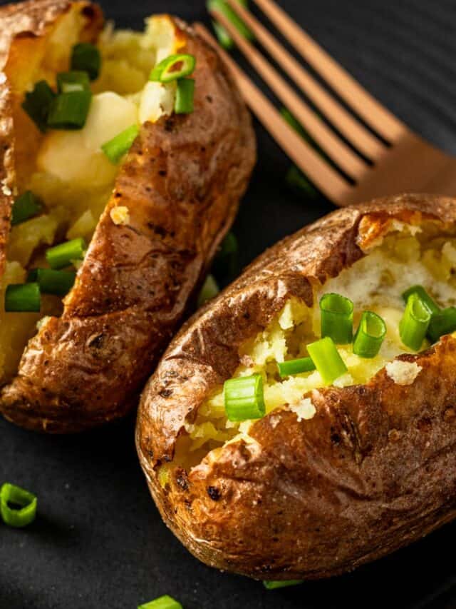 two air fryer baked potatoes cut in half topped with melting butter and chopped green onions.