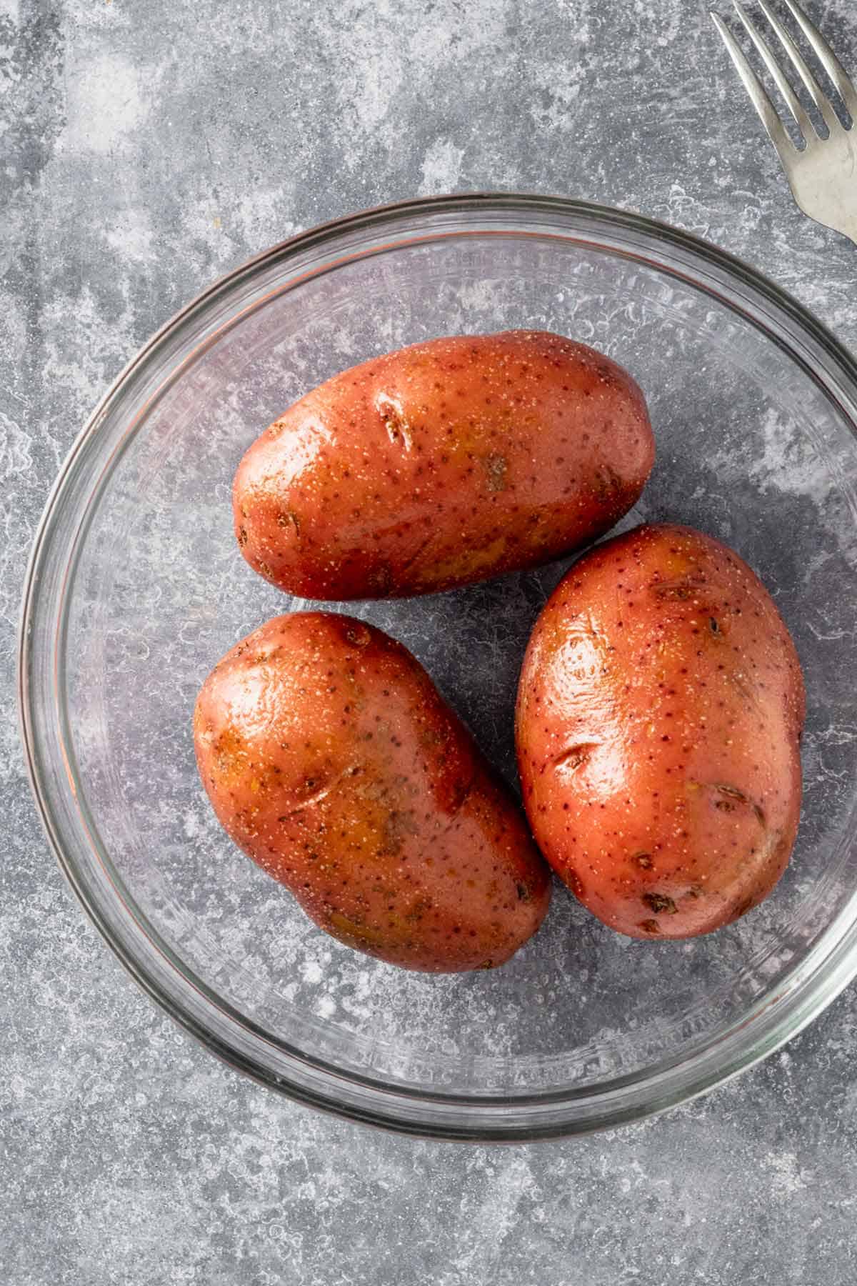 three whole potatoes with skins in a glass bowl.